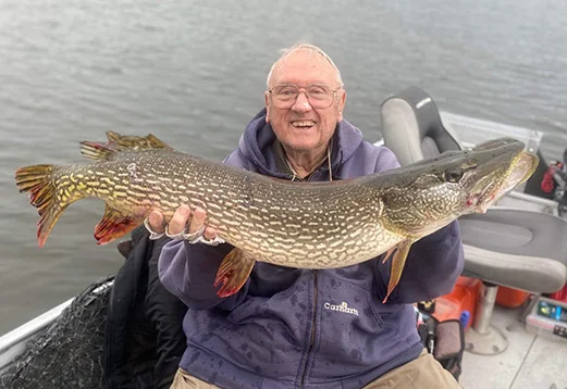 Older gentleman displaying big northern pike he caught on the lake